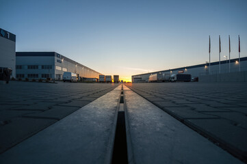 Logistics area with halls and trucks at sunset. Transport and storage of goods.