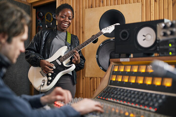 Portrait of black young woman playing electric guitar while composing music in professional...