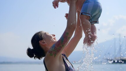 Happy young mom throws up baby in the pool. The development of kids. Bright light is shines from the windows of the indoors swimming pool little fun kid on vacation relax at swim pool, summertime