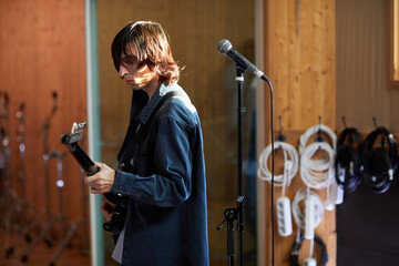 Portrait of young man playing guitar alone while practicing in music studio with sun accent, copy...
