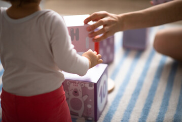 baby girl play toys with mother at home blurred background, view from behind