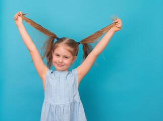 Happy excited jumping girl smiling with long hair ponytails on blue background.