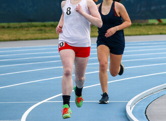 Two young girls running a race on a blue track