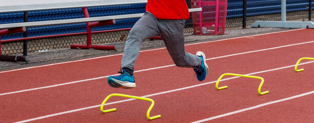 Obraz premium Side view of runner running over small yellow hurdles on a track