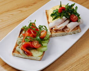 two sandwiches with salmon and avocado, ham and cheese and tomatoes
