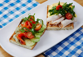 two sandwiches with salmon and avocado, ham and cheese and tomatoes