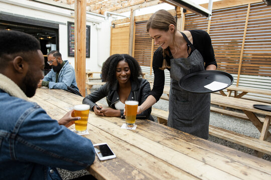 Cheerful bartender serving beer to happy customer in brewpub