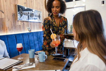 Restaurant manager placing cocktail on table for customer