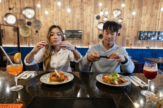 Couple taking photograph of dishes on bar counter