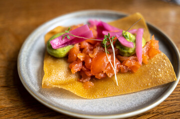 Mexican food, fried corn tortilla with smoked salmon, guacamole sauce and pink pickled onions