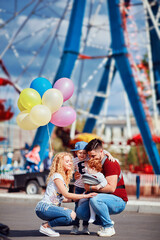 young family with kids having fun on funfair, amusement park at summer day with ferris wheel on background