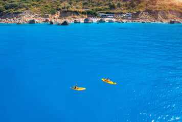Aerial view of yellow kayaks in blue sea at sunset in summer. Man and woman on floating canoe in...