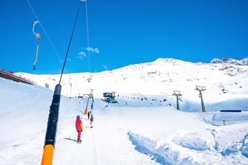 Fotobehang Tourists using drag lift for skiing. Beginners enjoying on snow covered landscape. White mountains against blue sky during sunny day. © ingusk