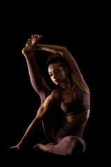 Fit woman practicing yoga poses. Side lit half silhouette girl doing exercise in studio against black background..
