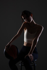 Teenage girl with basketball. Side lit studio portrait against dark background..