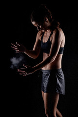 Fototapeta na wymiar Kickboxer kirl with magnesium powder on her hands punching with dust visible..