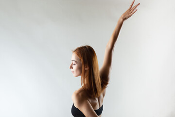 Beautiful girl with burnt orange hair stretching and making ballet pose. Studio portrait on gray background..