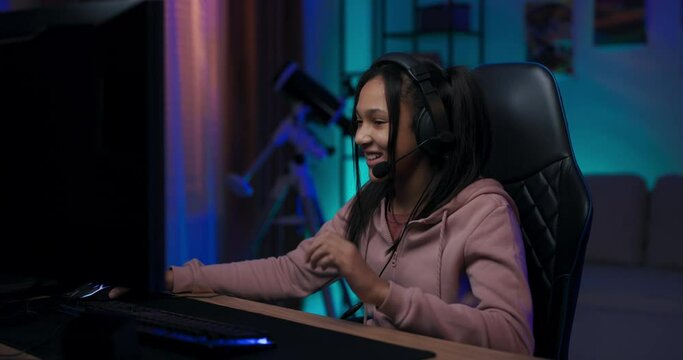 A professional young gamer prepares in room lit by blue and purple LEDs for an online e-sports championship, she puts on a headset, hijacks a keyboard and a mouse to play games.