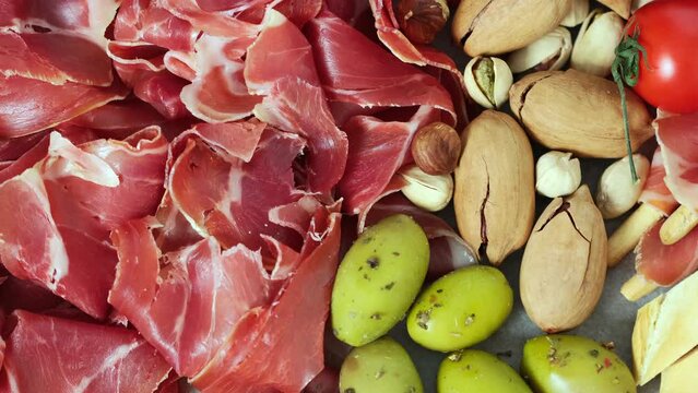 Meat appetizer selection - sliced prosciutto, sausage, ham, boiled pork balyk jamon sandwich cheese salami bread sticks olives tomatoes. Meat platter rotating View from above Slow motion Flat lay