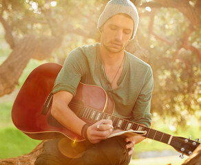 Lyrics inspired by nature. Shot of a handsome young man sitting in a park with a guitar writing...