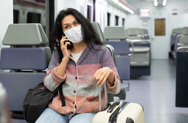 Young adult woman passenger wearing face mask for disease protection sitting in intercity train and...