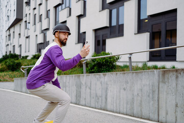  A man rides a skateboard and looks at a cell phone. Modern building in background