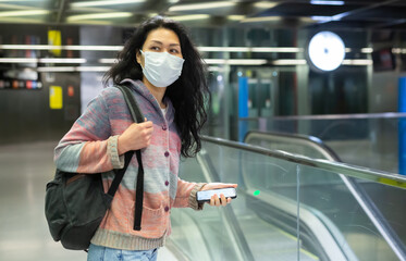 Fototapeta premium Asian woman in face mask with backpack walking in subway beside escolator