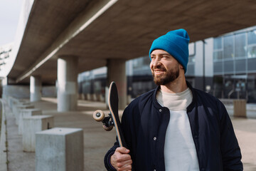 Trendy cool men portrait holding skate board and wearing cap. Skateboard spot. Copy space