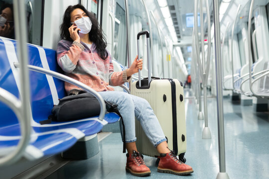 Portrait of young adult woman in protective face mask commuting in city using tube and talking on smartphone