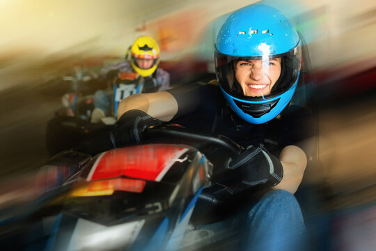 Glad smiling girl and her friends competing on racing cars at kart circuit