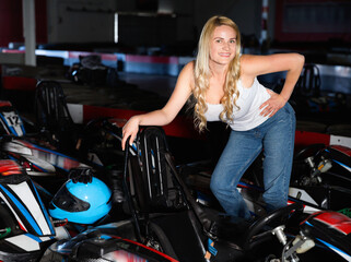 Fototapeta na wymiar Cheerful young pleasant beautiful positive caucasian woman near racing cars at kart circuit