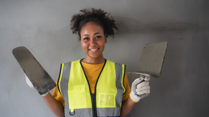 Portrait of an attractive African-American woman standing with plastering tool. The back is grey cement wall.
Female worker,wall decoration specialist.Smiling confidently.
expert skim coat,plastering - obrazy, fototapety, plakaty
