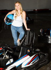 Fototapeta na wymiar Smiling woman with helmet standing near cars for karting in sport club