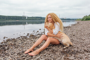 Fototapeta na wymiar Young woman sitting with her labrador retriever dog on the river shore