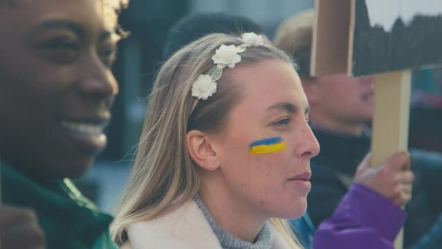 Close up of protestors with Ukranian flag painted on faces holding placards and chanting slogans on demonstration march in city - shot in slow motion