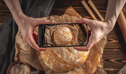 A baker is taking pictures of homemade fresh bread on his phone for a post on social networks....