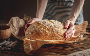Female hands holding homemade natural bread with a Golden crust on a napkin on an old wooden background. Rustic style