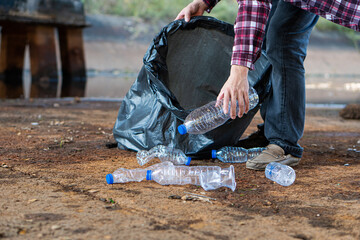 The young man's hand held various plastic bottles in a black bag. They are piled together to be sold to buyers who collect them for recycling. waste separation concept for recycling