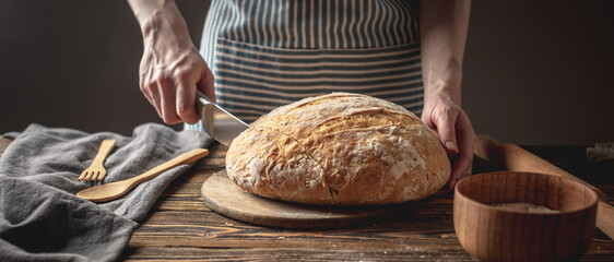 Hands cut with a knife homemade natural fresh bread with a Golden crust on wooden background....