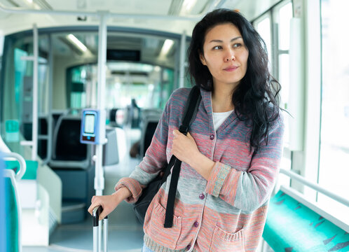 Positive female passenger using public transport in big city, moving in tram