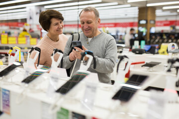 Middle aged wife and husband picking new smartphone in electronic store.