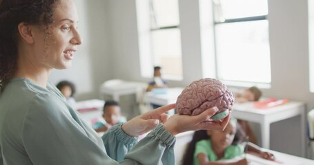 Video of happy caucasian female teacher holding brain model in class of diverse pupils - Powered by Adobe