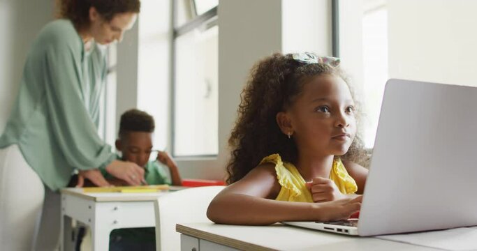 Video of focused african american girl sitting at desk with laptop during lesson in classroom