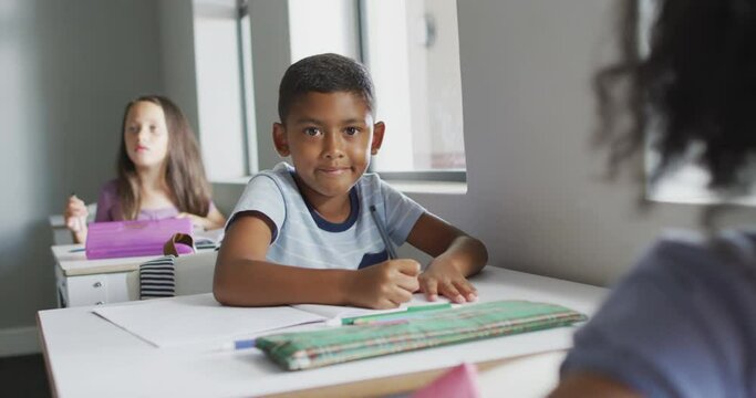 Video of happy biracial boy sitting at desk in classsroom