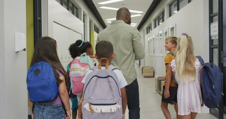 Video of back of african american male teacher and diverse pupils walking at school hall - Powered by Adobe