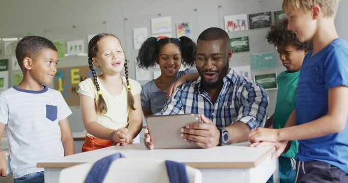 Video of happy african american male teacher and class of diverse pupils working on tablet