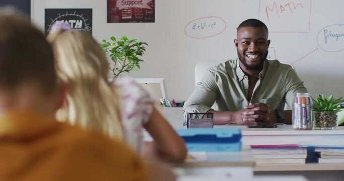 Video of happy african american male teacher sitting at desk during math lesson