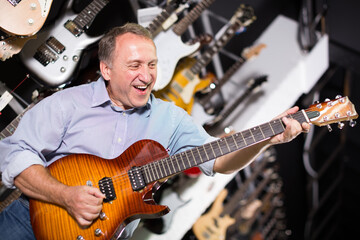 Obraz premium Smiling musician is playing on modern electric guitar in music shop.