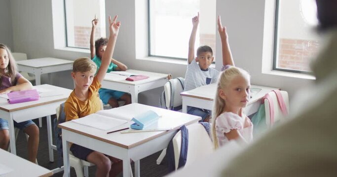 Video of diverse pupils raising hands during lesson in classsroom