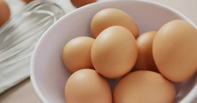 Video of close up of eggs and egg whisk on rustic cloth on beige background